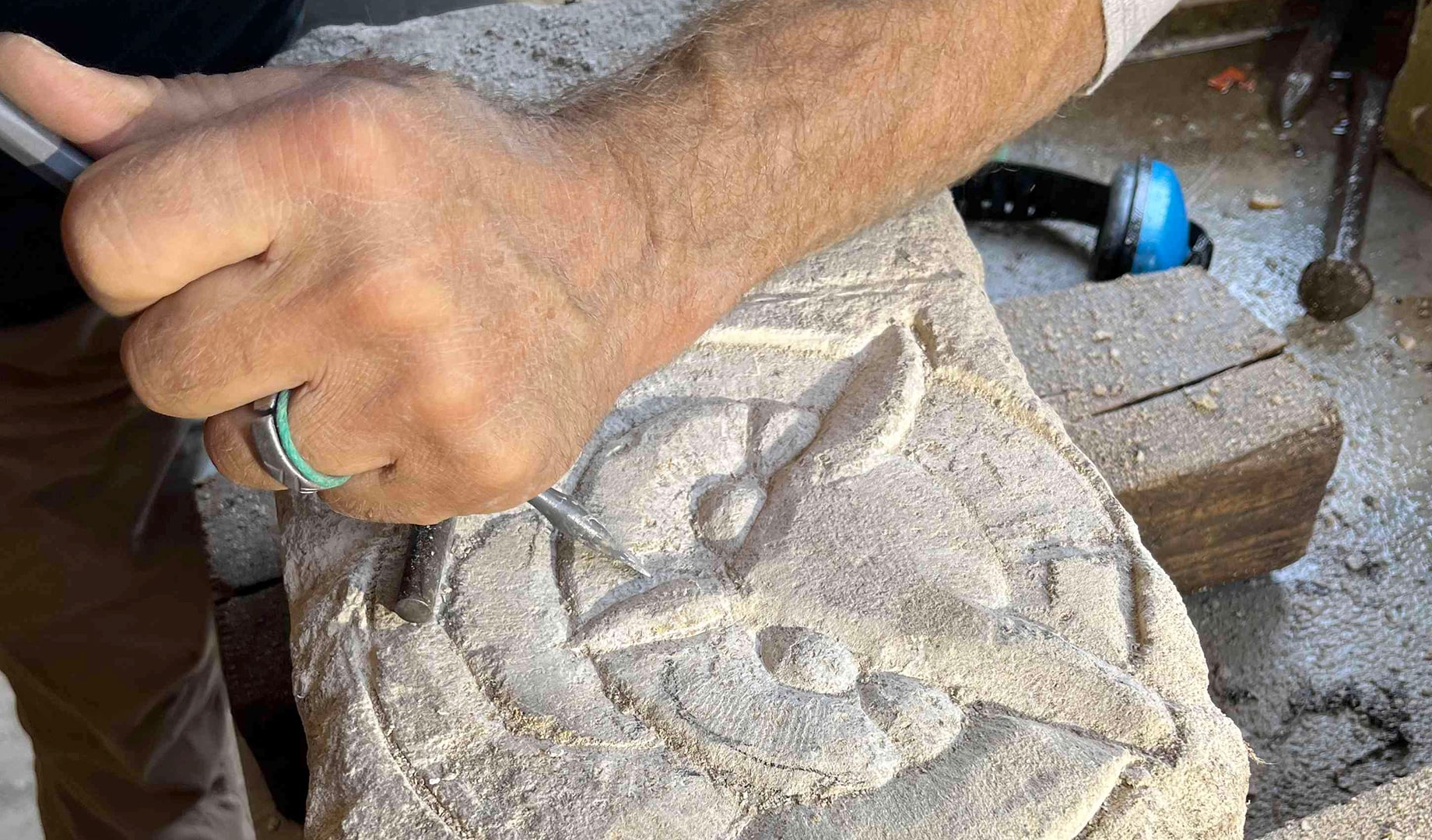 A hand with a metal tool carves an owl into a stone.